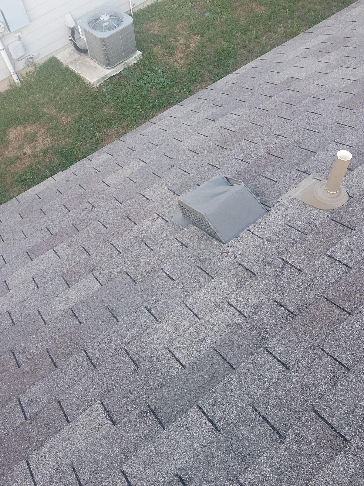Hail-damaged static roof vent with a split corner seam beside a pipe boot