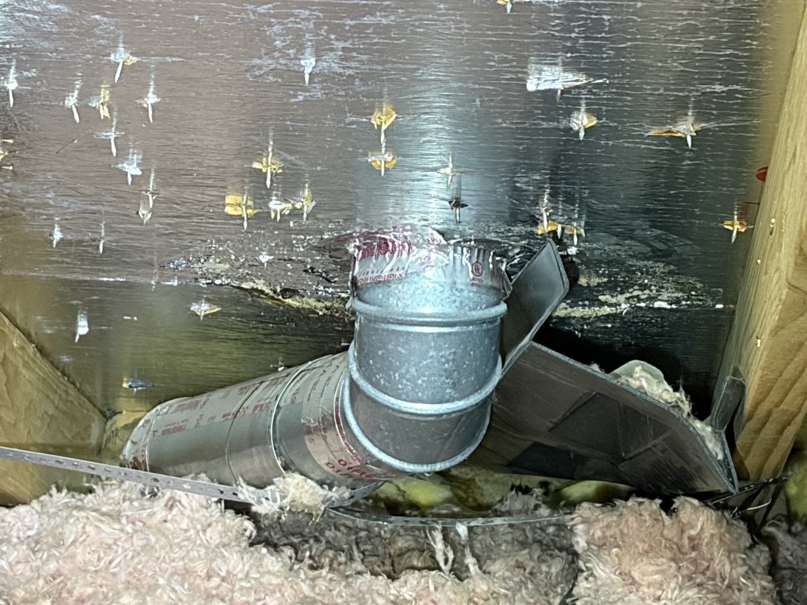 Attic view of a Master Flow pipe boot hanging from a dryer vent leak path.